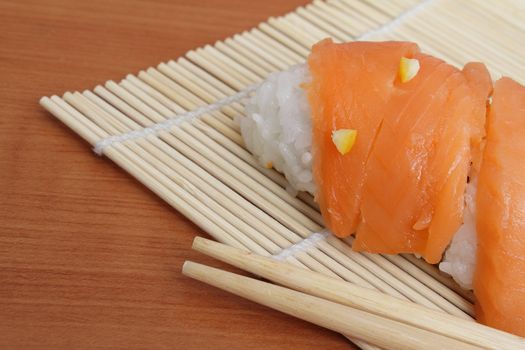 Closup photo of salmon sushi and chopsticks on bamboo mat
