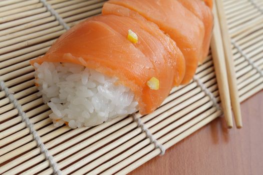 Closeup photo of salmon sushi and chopsticks on bamboo mat