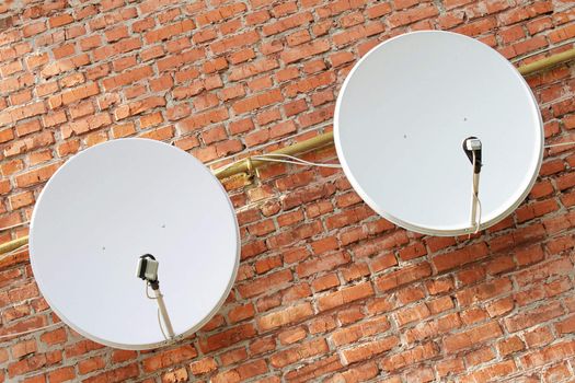 Two satellite dishes on the brick wall