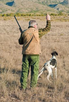 Quail hunter in camouflage clothing walking across the field