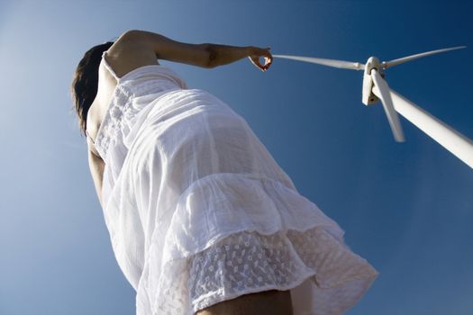 Crazy perspective of a young woman with white dress trying to touch the blade of a windmill.