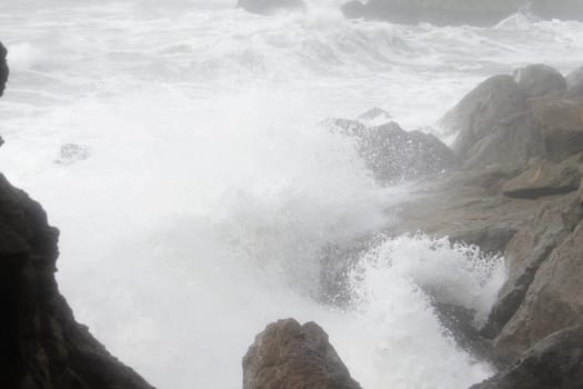 Ocean waves break over rocky coastline in foggy day