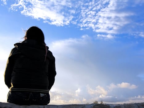 young girl sitting on wall watching the cloudy sky.