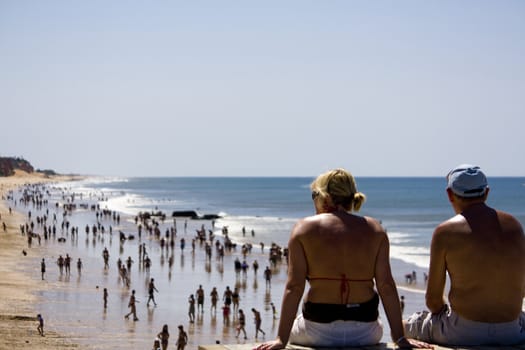 View of a middle age couple gazing the crowded beach shoreline.