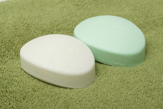 Two bars of soap, white and green, on green bath towel
