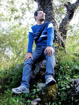 Young man sitting on a rock in front of a tree apreciating the nature.