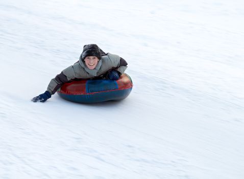 boy sledding down a snowy hill on a color inflatable sled