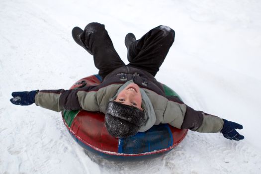 boy sledding down a snowy hill on a color inflatable sled