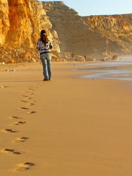 young woman walking on the Tonel Beach near Sagres, Portugal, leaving a footstep trail on the sand.