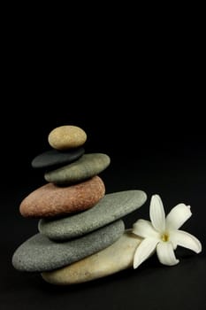 Seven pebbles pyramid in staggered rows, with a white flower, over black