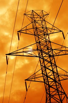 The silhouette of a power line tower against an ominous orange sky.