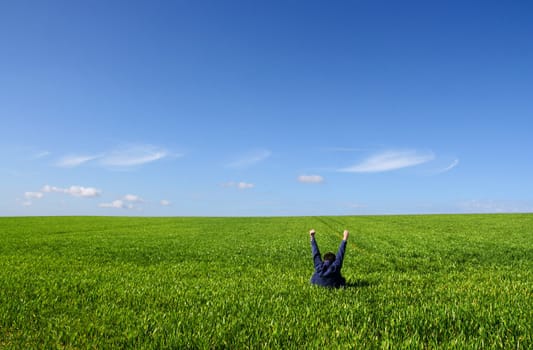 A man sitting alone in a green field, with lifted V arms