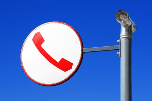 Round sign with telephone against blue sky