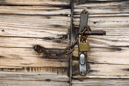 Old wooden gate locked with chain and padlock to handle