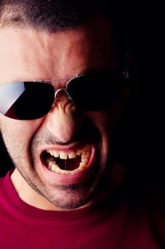 Close detail view of a angry young male man with dark shades isolated on a black background.