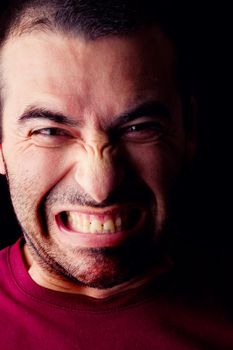 Close detail view of a furious young male man isolated on a black background.