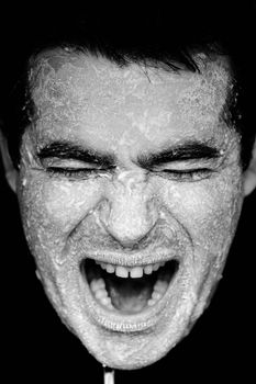 Close up view of a man's hands on the face covered in flour, screaming.