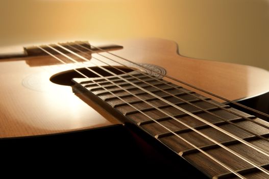 Close and low level angle capturing an acoustic guitar with warm brown background. Focus on foreground strings.