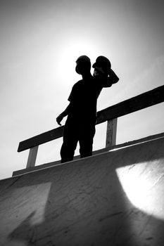 Silhouette of a young teenage skateboarder at the top of the half pipe ramp at the skate park.