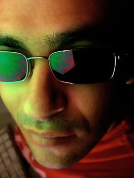 young man looking at camera with cool look next to computer on a nocturnal setting.