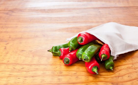 Fresh green and red chilli peppers in a cloth bag, displayed on a beautiful wooden table