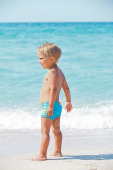 Cute little boy stands in front of the blue sea