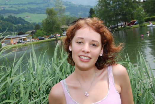 Beautiful red haired woman smiling at little lake in summer.