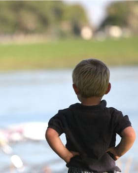 Little boy with hands on hips looking out over water
