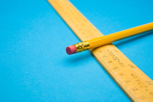 Yellow wooden ruler and pencil on blue background