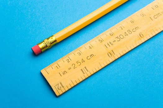 Wooden ruler and pencil laying on blue background