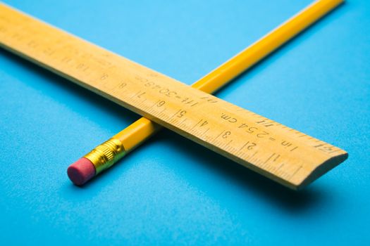 Wooden ruler and pencil crossed on blue background