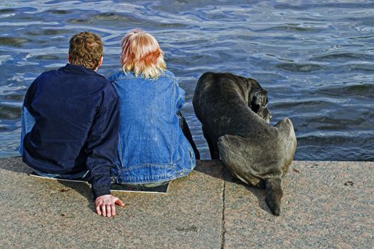 A couple and a dog sitting at the embankment of Neva river in Saint Petersburg, Russia.