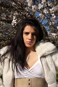 View of a beautiful girl on a white dress on a green grass field next to a almond tree