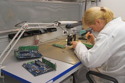 Engineer working with circuits - A woman engineer solders circuits sitting at a table.