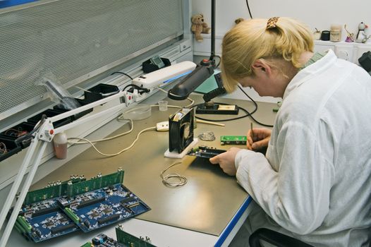 A woman engineer solders circuits sitting at a table.