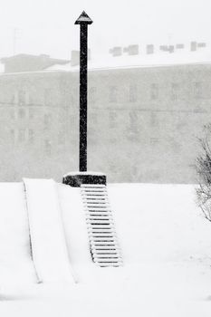 Benches at a back alley while snowing heavily.