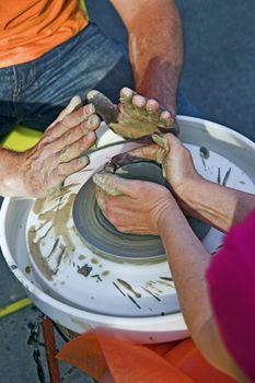 potter's hands guiding woman's hands to help her learn pottery