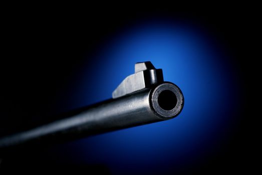 Gun barrel on black background at angle back lit by blue spot