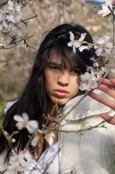 View of a beautiful girl on a white dress on a green grass field next to a almond tree