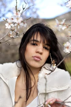 View of a beautiful girl on a white dress on a green grass field next to a almond tree