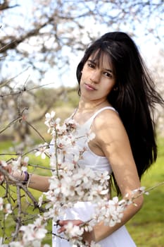 View of a beautiful girl on a white dress on a green grass field next to a almond tree