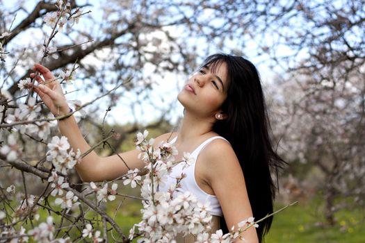 View of a beautiful girl on a white dress on a green grass field next to a almond tree