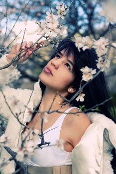 View of a beautiful girl on a white dress on a green grass field next to a almond tree