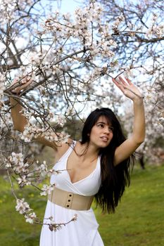 View of a beautiful girl on a white dress on a green grass field next to a almond tree