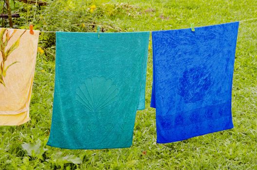 Multicolor towels atached with pins hanging on string in farmstead. Wooden fence in background.