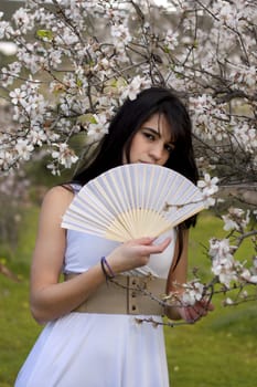 View of a beautiful girl on a white dress on a green grass field next to a almond tree