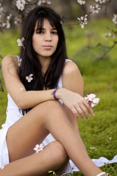 View of a beautiful girl on a white dress on a green grass field next to a almond tree