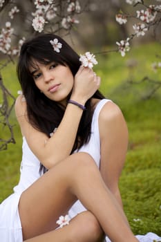 View of a beautiful girl on a white dress on a green grass field next to a almond tree