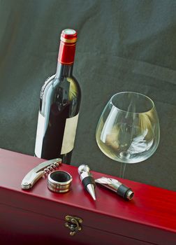Bottle of red wine near a wooden box, with wine tools amd a glass