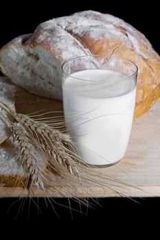 Glass of milk, wheat and bread over wooden plate